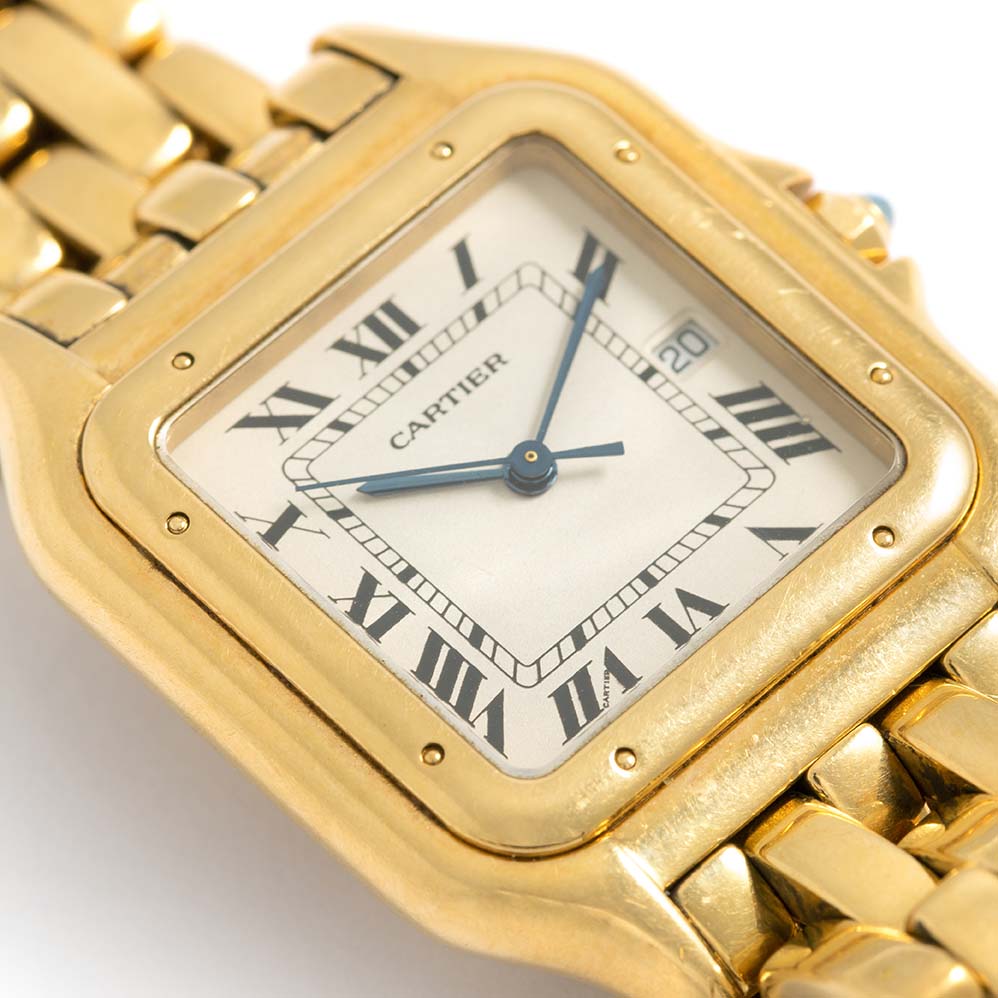 Close-up of the Cartier Panthere Large Mens Watch. 29mm 18K yellow case with 18K yellow gold bezel. Off-white dial with blue steel hands and black Roman numeral hour markers. Date display at the 3 o'clock position. Minute markers on the inner dial. 18K yellow gold bracelet with a hidden butterfly clasp. Will fit up to a 6.5-inch wrist.