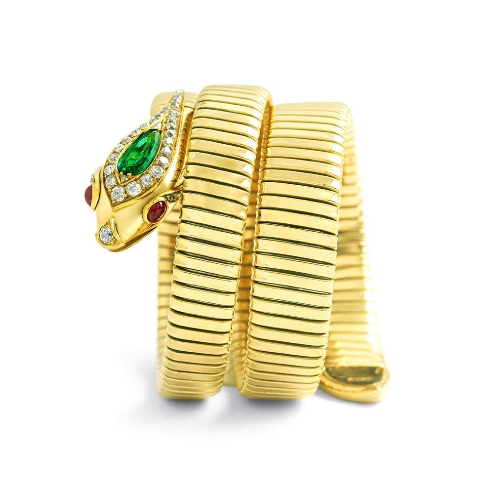 Front view of a Snake Tubogaz bracelet in yellow gold. On the head is a large pear-shaped emerald surrounded by diamonds. The eyes are made of two rubies and the nose is made of a diamond.