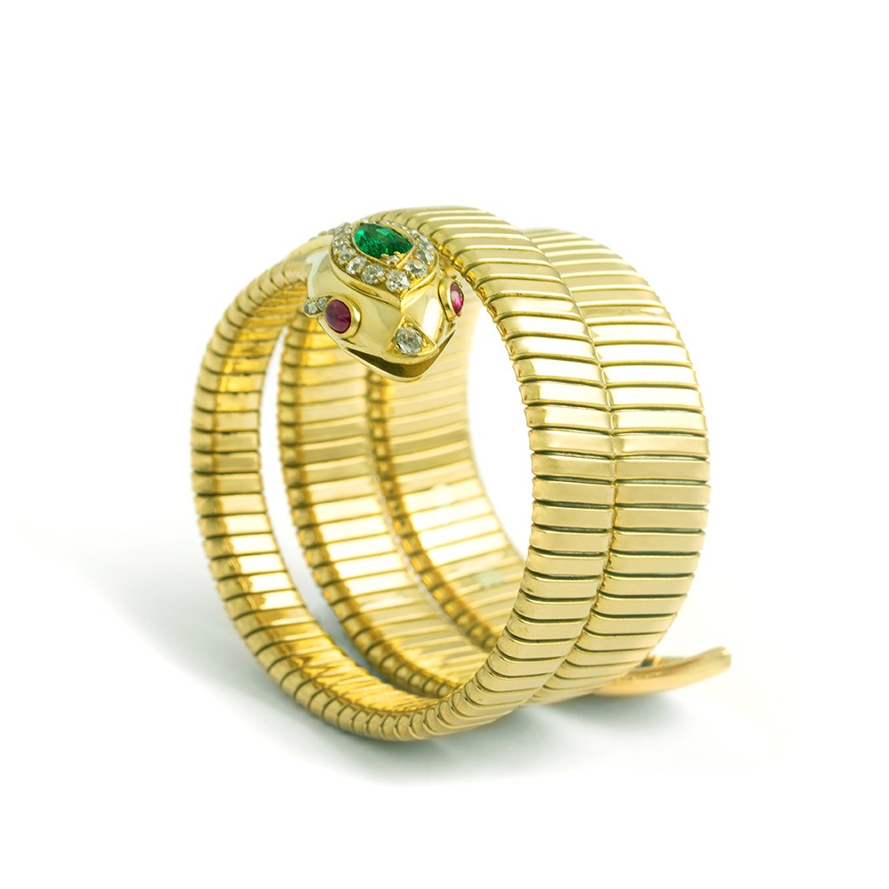 Side view of a Snake Tubogaz bracelet in yellow gold. On the head is a large pear-shaped emerald surrounded by diamonds. The eyes are made of two rubies and the nose is made of a diamond.
