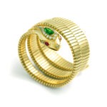 Side view of a Snake Tubogaz bracelet in yellow gold. On the head is a large pear-shaped emerald surrounded by diamonds. The eyes are made of two rubies and the nose is made of a diamond.